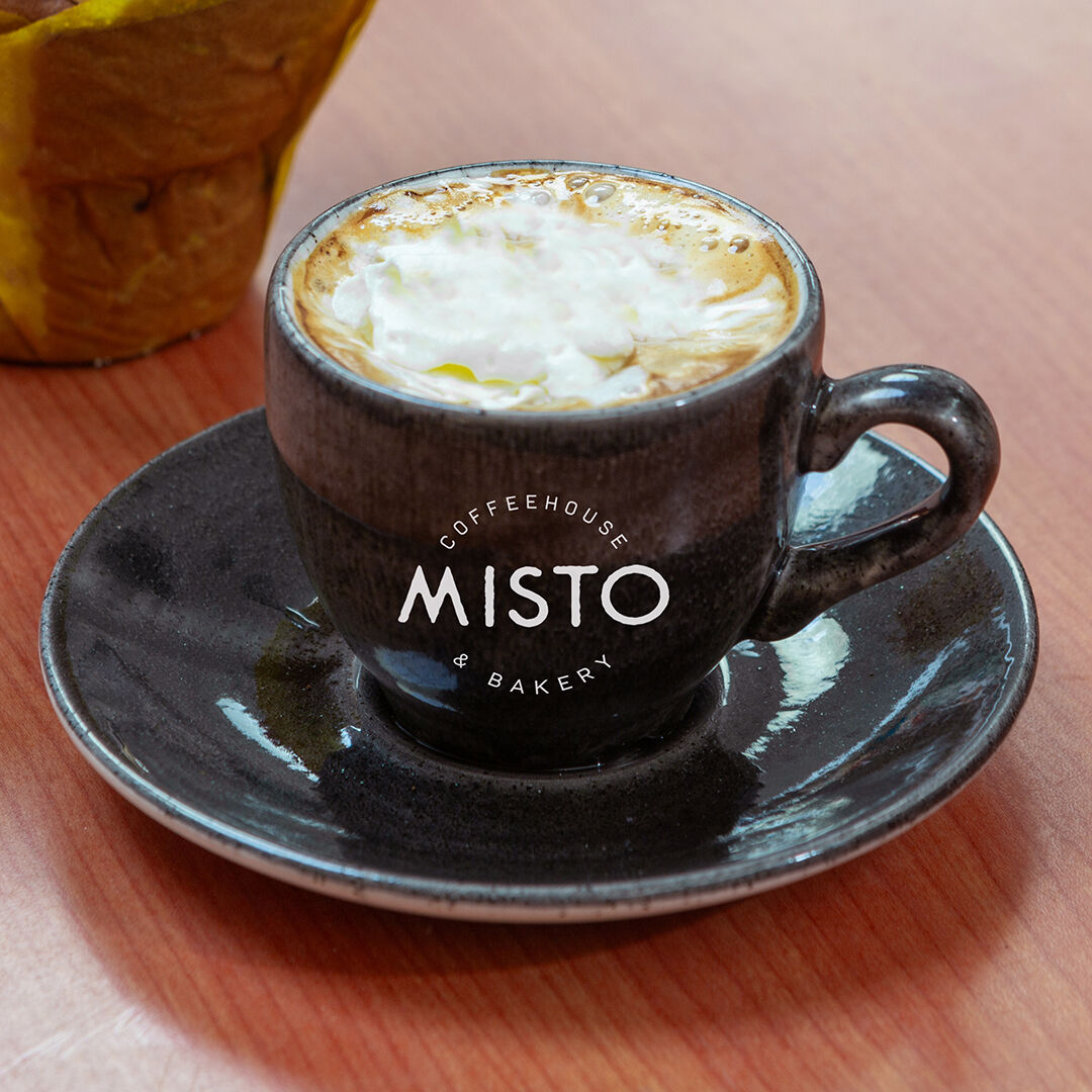 A cappuccino with cream in a dark speckled Misto cup and saucer.