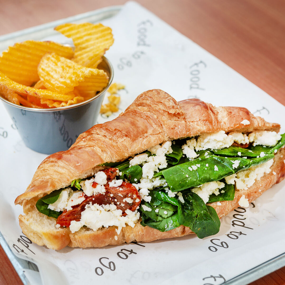 A filled croissant with spinach, feta and sun-dried tomato, with crisps.