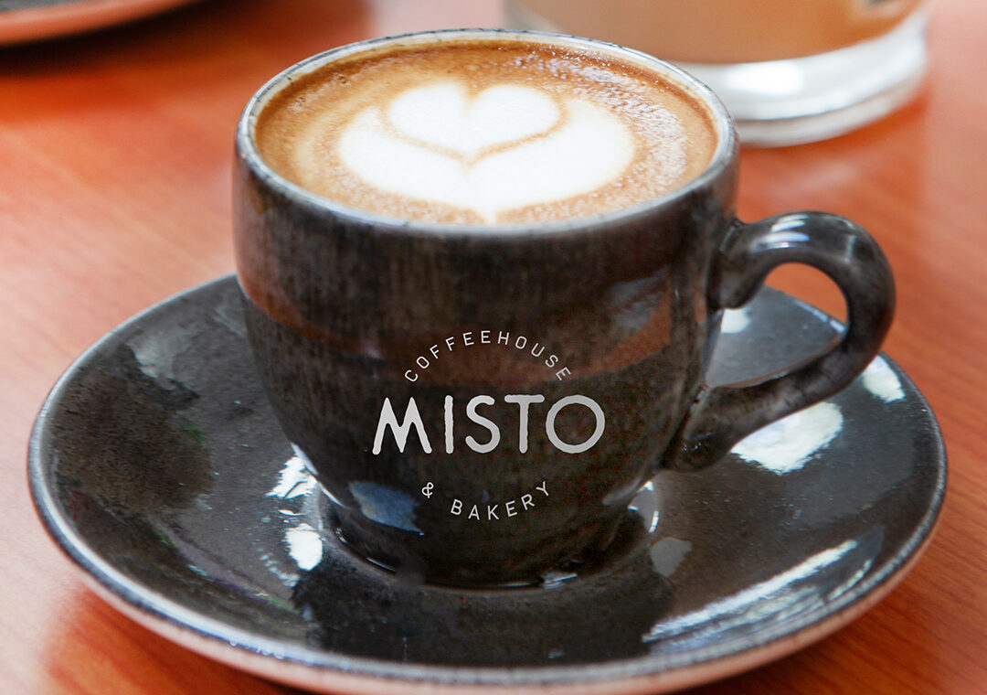 A Misto espresso cup and saucer with heart latte art, a glass Misto mug behind it.